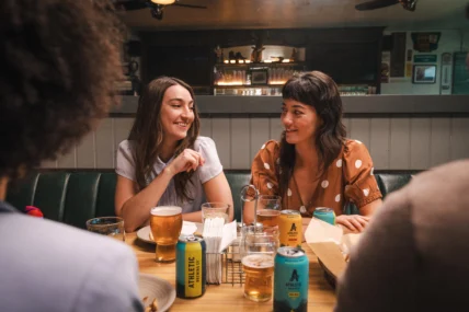 Friends socializing at a bar while drinking Athletic Brewing non-alcoholic beer, highlighting alcohol-free craft beer in a casual dining setting