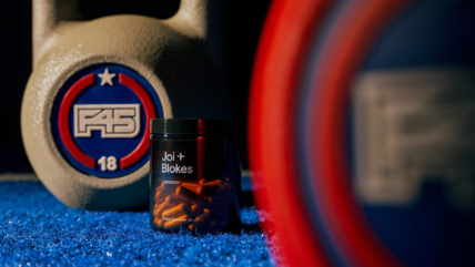 A container of Joi + Blokes supplements placed on a gym floor between F45-branded kettlebells and weight plates.