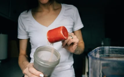 woman powers protein powder into a shaker bottle